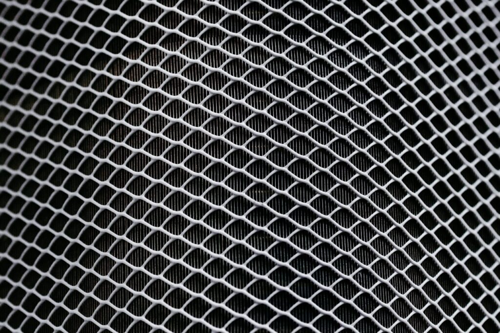 Detailed texture of industrial metal mesh with geometric patterns and shadows.